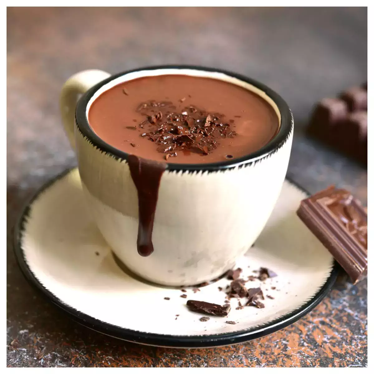 A small, white coffee cup on a coaster with a square of chocolate leaning on the coaster. A small drip of coffee slides down the cup.