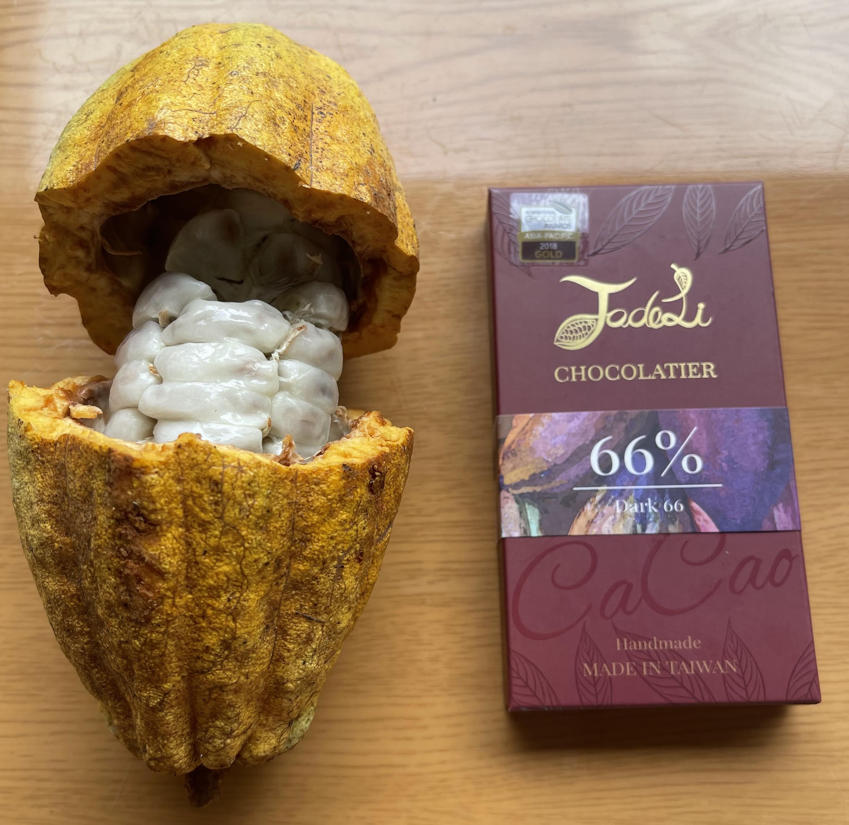 A ripe yellow cacao pod broken open to reveal the white flesh, next to a dark red chocolate bar made from the bean.